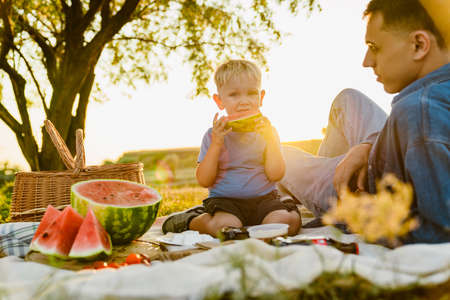 Young white father and son eating watermelon during picnic on summer fieldの写真素材