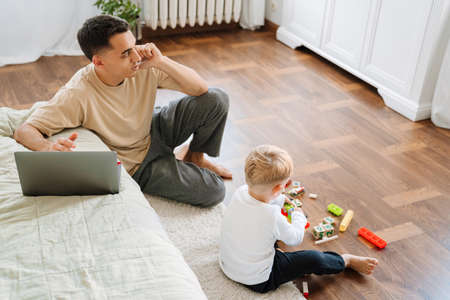 Young father talking on cellphone while spending time with his son at home