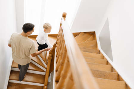 White man and his son coming up wooden stairs at homeの写真素材