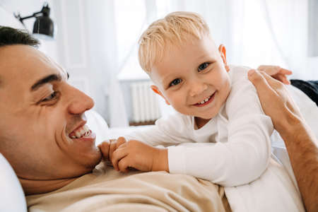 Young white father making fun and playing with his son on bed at home