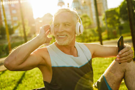 Grey man listening music and using cellphone while sitting on grass outdoors