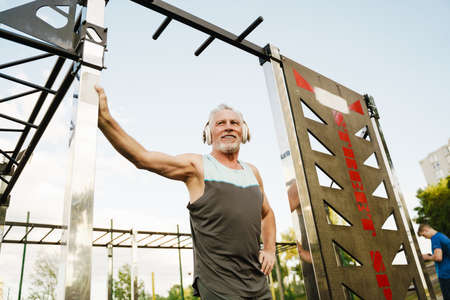 Grey senior sportsman listening music while working out on sports ground