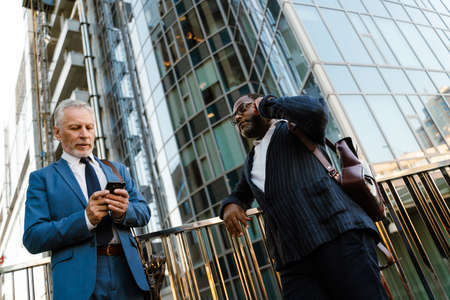 Multiracial men talking and using cellphones while standing by building outdoorsの写真素材