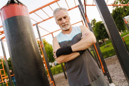Grey senior man in boxing bandage working out on sports ground
