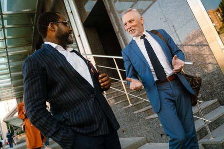 Multiracial men dressed in suits talking and gesturing while going down stairs outdoors