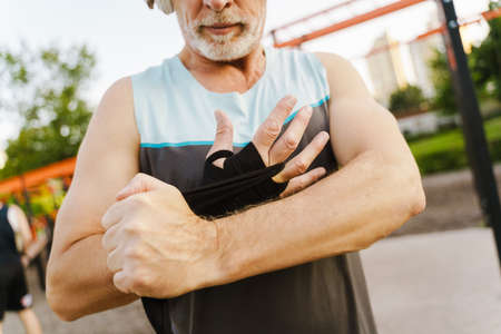 Grey senior man listening music while wrapping his hand boxing bandage on sports ground