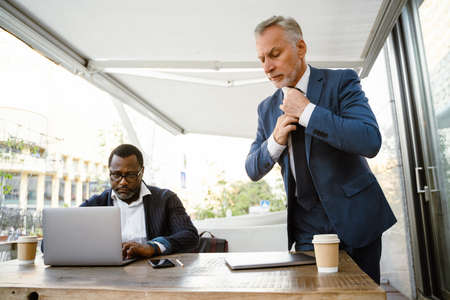 Multiracial men wearing jackets working with laptops in cafe outdoors
