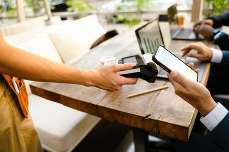 White man paying with cellphone while working with colleague in cafe outdoors