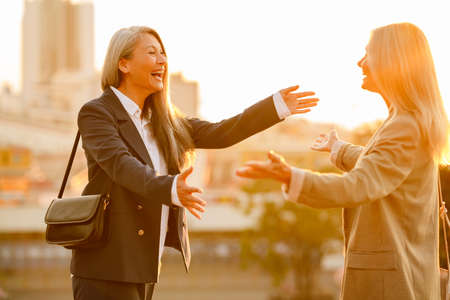 Mature multiracial businesswomen laughing and hugging during meeting outdoors