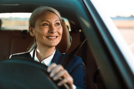Mature asian businesswoman with grey hair smiling while driving car