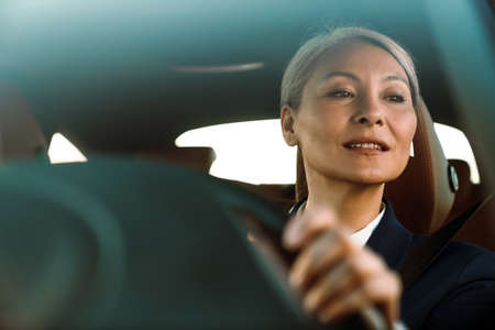Mature asian woman with grey hair using earphone while driving carの写真素材