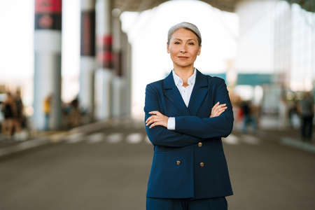 Grey asian woman wearing suit posing on airport parking outdoors