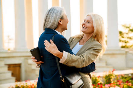 Mature multiracial businesswomen laughing and hugging during meeting outdoorsの写真素材