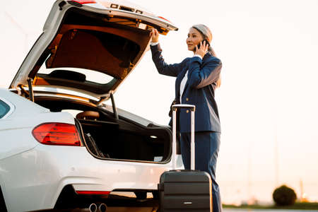 Mature asian businesswoman talking on cellphone while opening trunkの写真素材