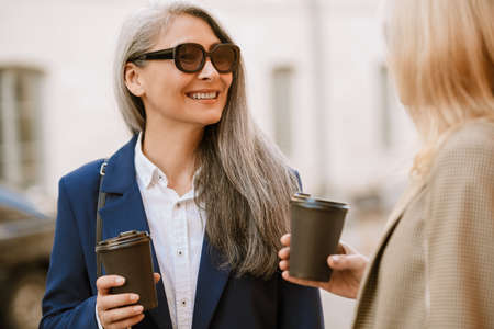 Mature multiracial women drinking coffee during meeting outdoorsの写真素材
