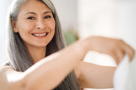 Mature asian woman with grey hair smiling and looking at camera at homeの写真素材