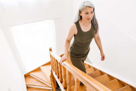 Mature asian woman with grey hair going up stairs at homeの写真素材