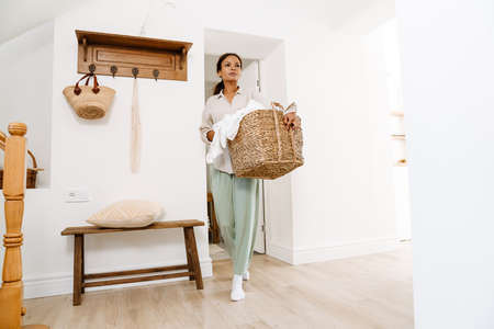 Black woman wearing pajama holding basket with clothes at homeの写真素材