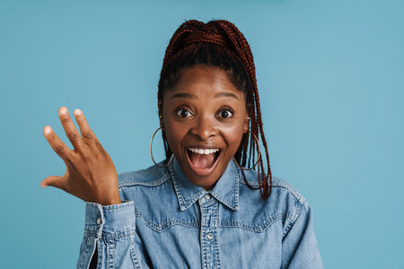 Young black woman with afro pigtails expressing surprise at camera isolated over blue background