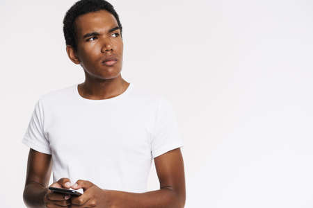 Young black man dressed t-shirt using mobile phone isolated over white wall