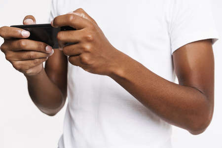Young black man playing online game on mobile phone isolated over white wall