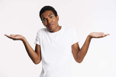 Young black man dressed t-shirt frowning while holding copyspace isolated over white wallの写真素材