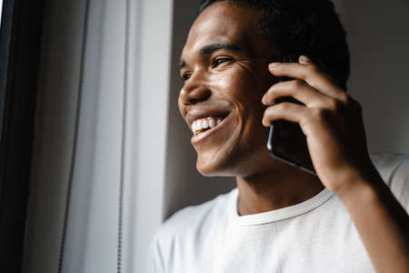 Young black man smiling and talking on cellphone while leaning on wall indoorsの写真素材