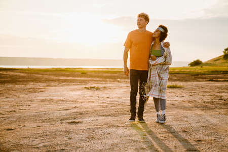 Young multiracial couple hugging and smiling while walking together outdoors