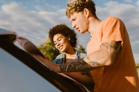 Young multiracial couple talking and examining map during car trip