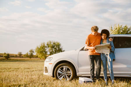 Young multiracial couple smiling and examining map during car trip