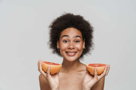 Black shirtless woman smiling while posing with grapefruit isolated over white backgroundの写真素材