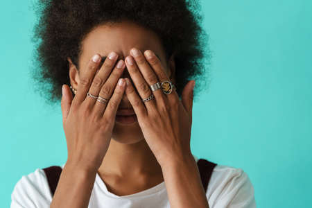 Black young woman wearing rings covering her eyes isolated over blue background