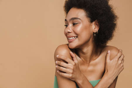 Black brunette woman smiling and looking at camera isolated over beige backgroundの写真素材