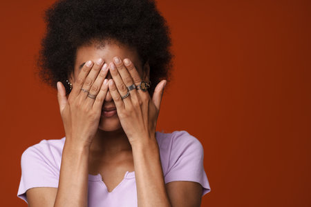 Black young woman wearing rings covering her eyes isolated over brown backgroundの写真素材