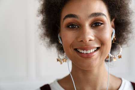 Black young woman smiling while listening music with earphones indoors