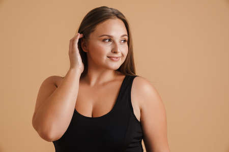 Young woman wearing swimsuit smiling and looking aside isolated over beige backgroundの写真素材
