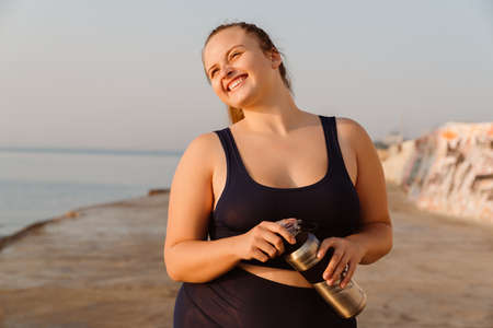 Ginger young woman drinking water during yoga practice outdoors
