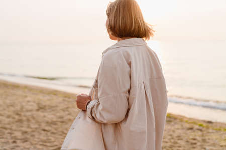Blonde european woman wearing shirt walking on sandy beachの写真素材