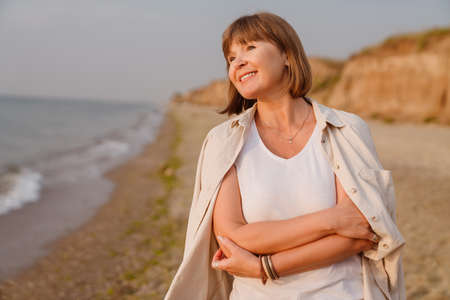Senior european woman smiling while walking on sandy beach
