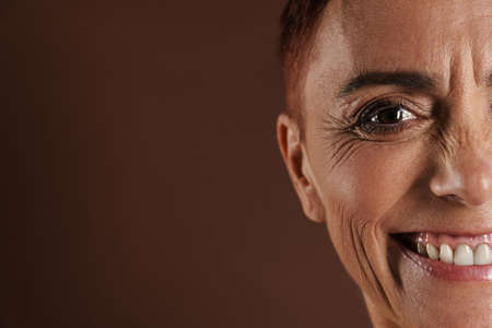 Senior shirtless woman smiling while posing on camera isolated over brown wall