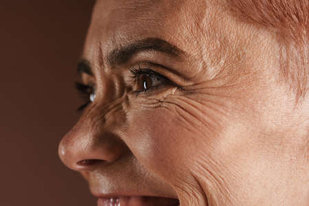 Senior shirtless woman smiling while posing on camera isolated over brown wall