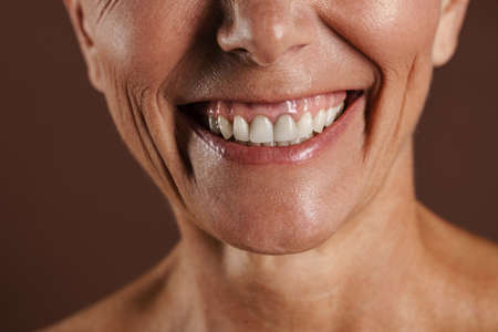 Senior shirtless woman smiling while posing on camera isolated over brown wall