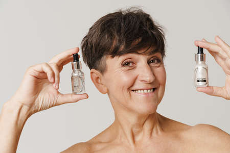 Mature half-naked woman smiling while showing cosmetic products isolated over white backgroundの写真素材