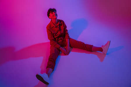 Mature european woman wearing shirt sitting on floor isolated over pink background