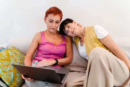 Mature lesbian couple using laptop while resting on sofa together at home