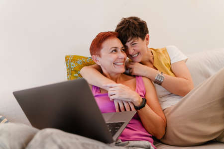 Mature lesbian couple hugging and using laptop on sofa at home