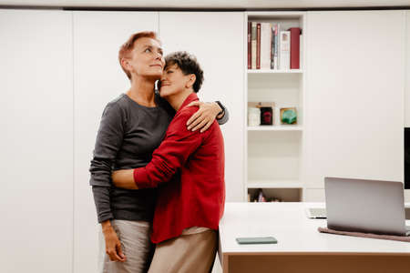 Mature lesbian couple hugging and smiling at homeの写真素材