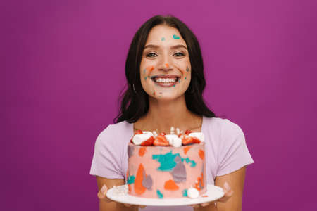 Young woman smiling while posing with birthday cake isolated over purple wall