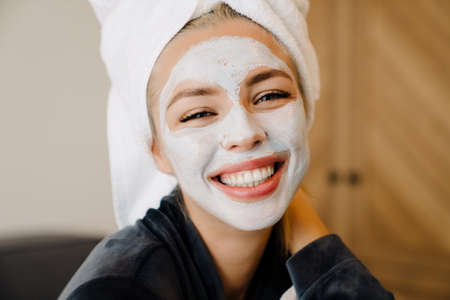 Young woman with face mask laughing while sitting in bed at home