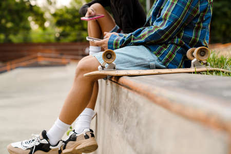 Two white teenagers using cellphones while spending time at skate park outdoorsの写真素材